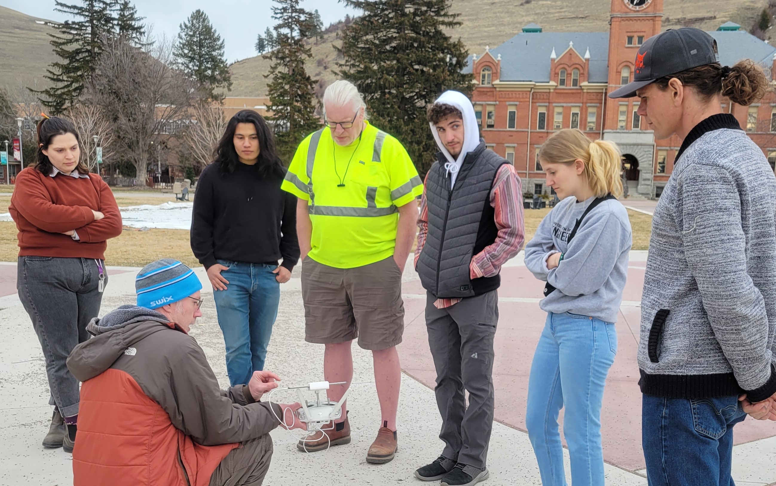 six people stand outside watching an instructor demonstrate a drone controller