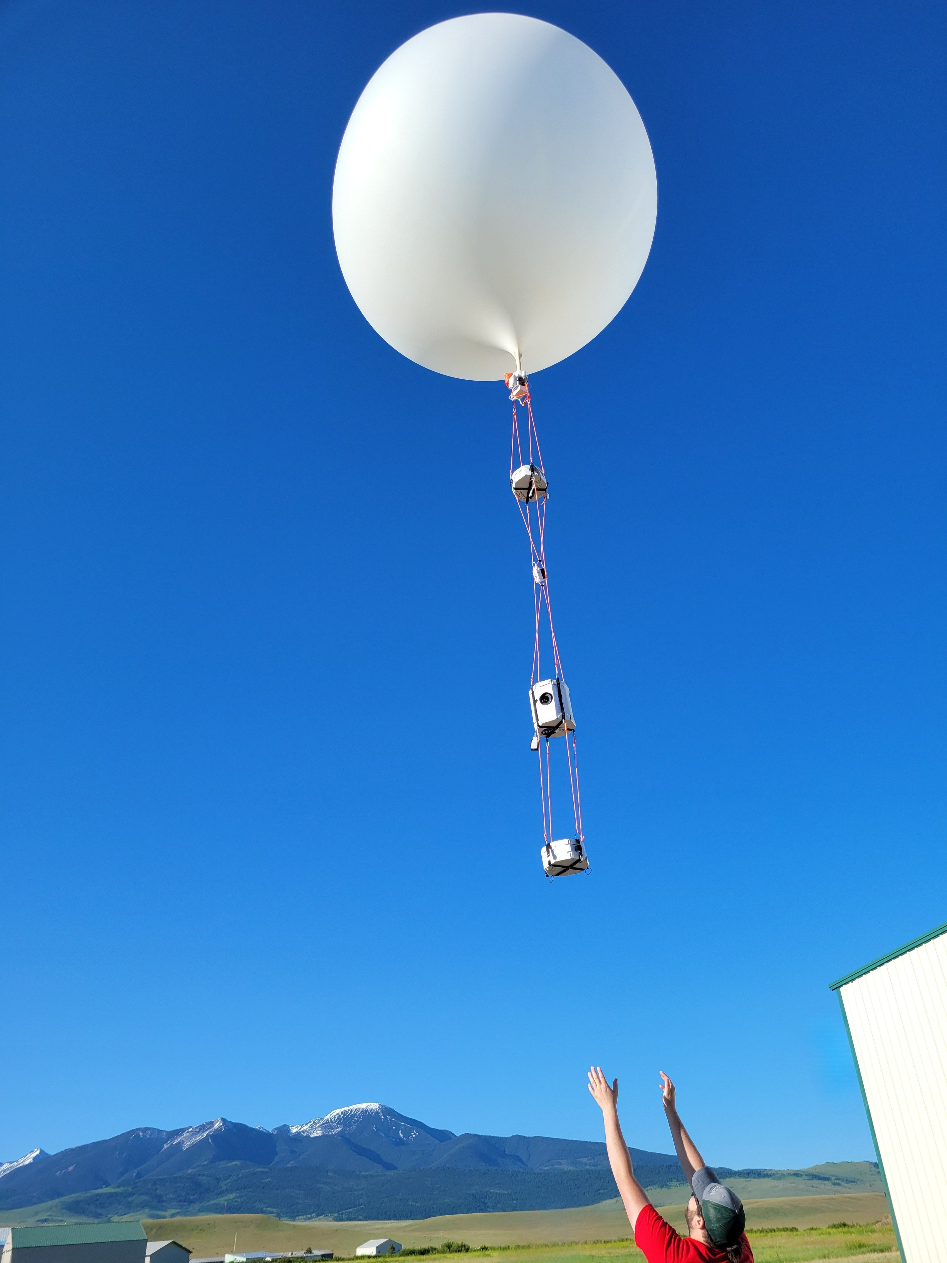 A large balloon with strings bellow carrying payloads being release by a boy
