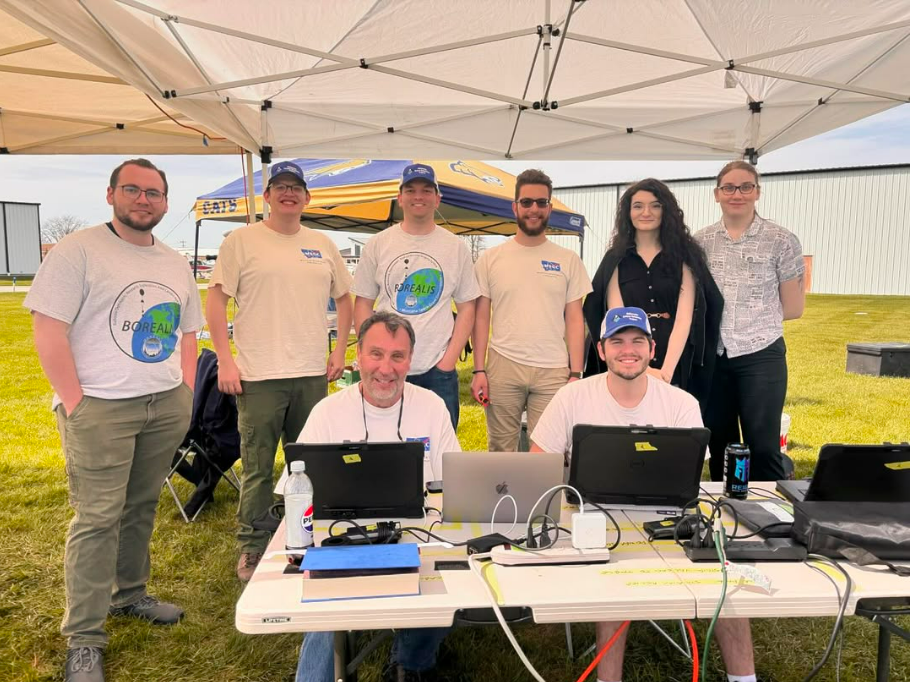 A group of people standing outside at a table with laptops