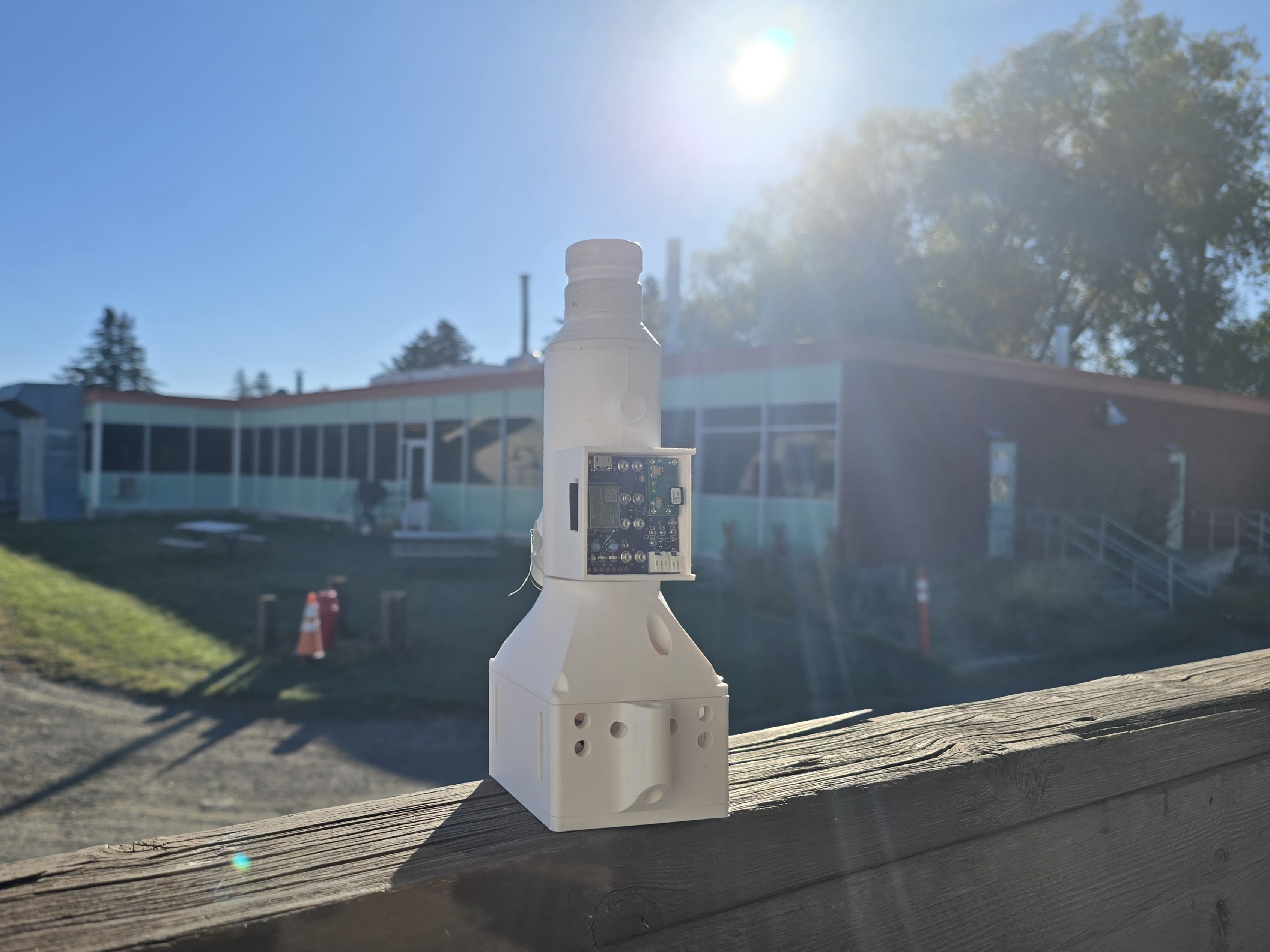 A white 3d printed device called the vent system with a purple board inside on a hand rail on a sunny day